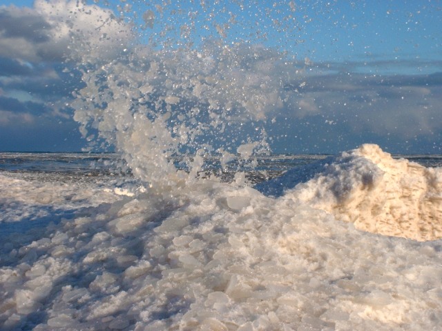 Ice and sand splashing high in the air when wave crashes into ice-bank