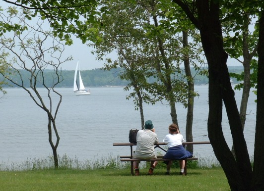 Tranquil scene of Sturgeon Bay & sailboat with spectators on park bench